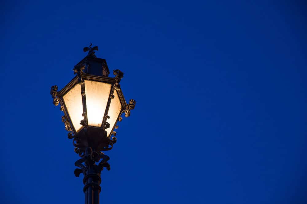 Lit black lamp post with dark blue sky background